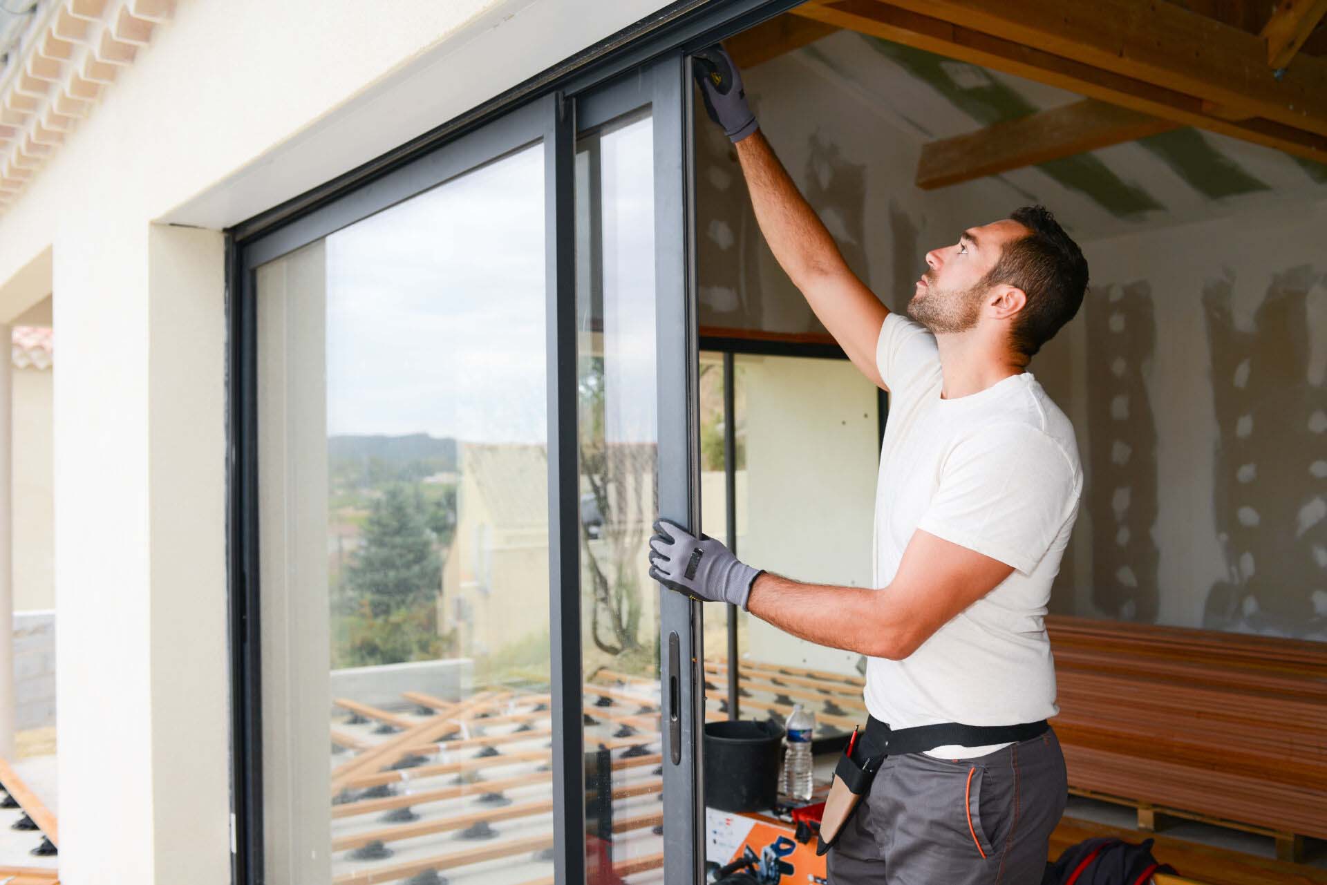 handsome young man installing a bay window in a new house construction site Insurance for Door and Window Installation Businesses