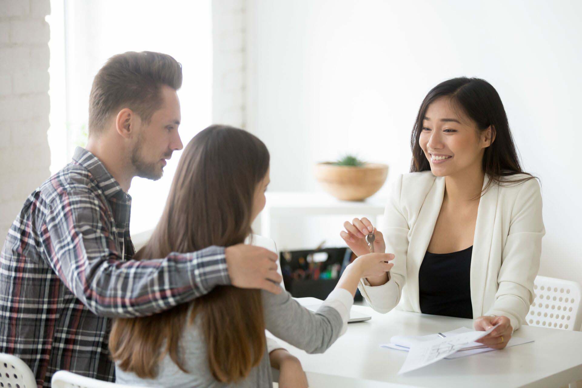Smiling broker giving keys from first house to millennial couple Insurance for Real Estate Agents and Brokers