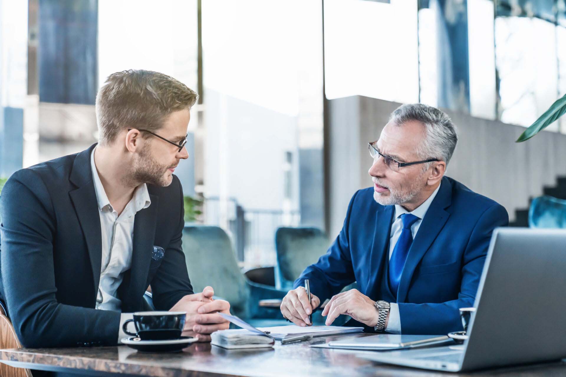 Horizontal shot of young executive showing his business proposal to a senior man sitting in foyer Insurance for Executive Coaches