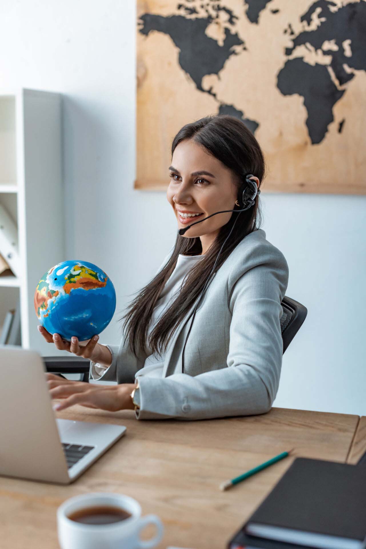 smiling travel agent holding globe while sitting at workplace Insurance for Travel Agents