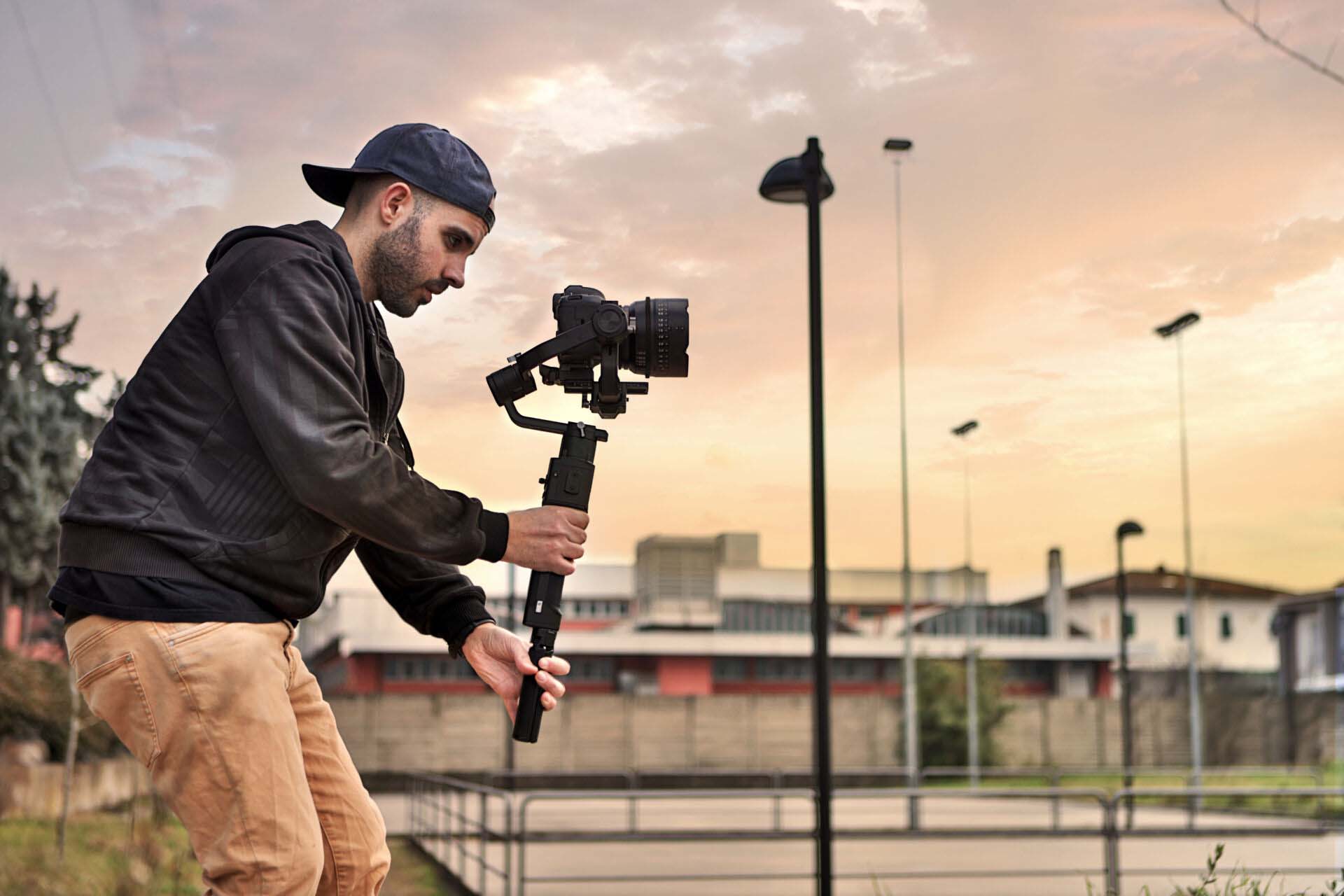 Caucasian videographer filming with cinema gimbal video dslr at sunset , professional video, videographer in event. Cinema lens on gimbal. Medium shot from right side Insurance for Videographers