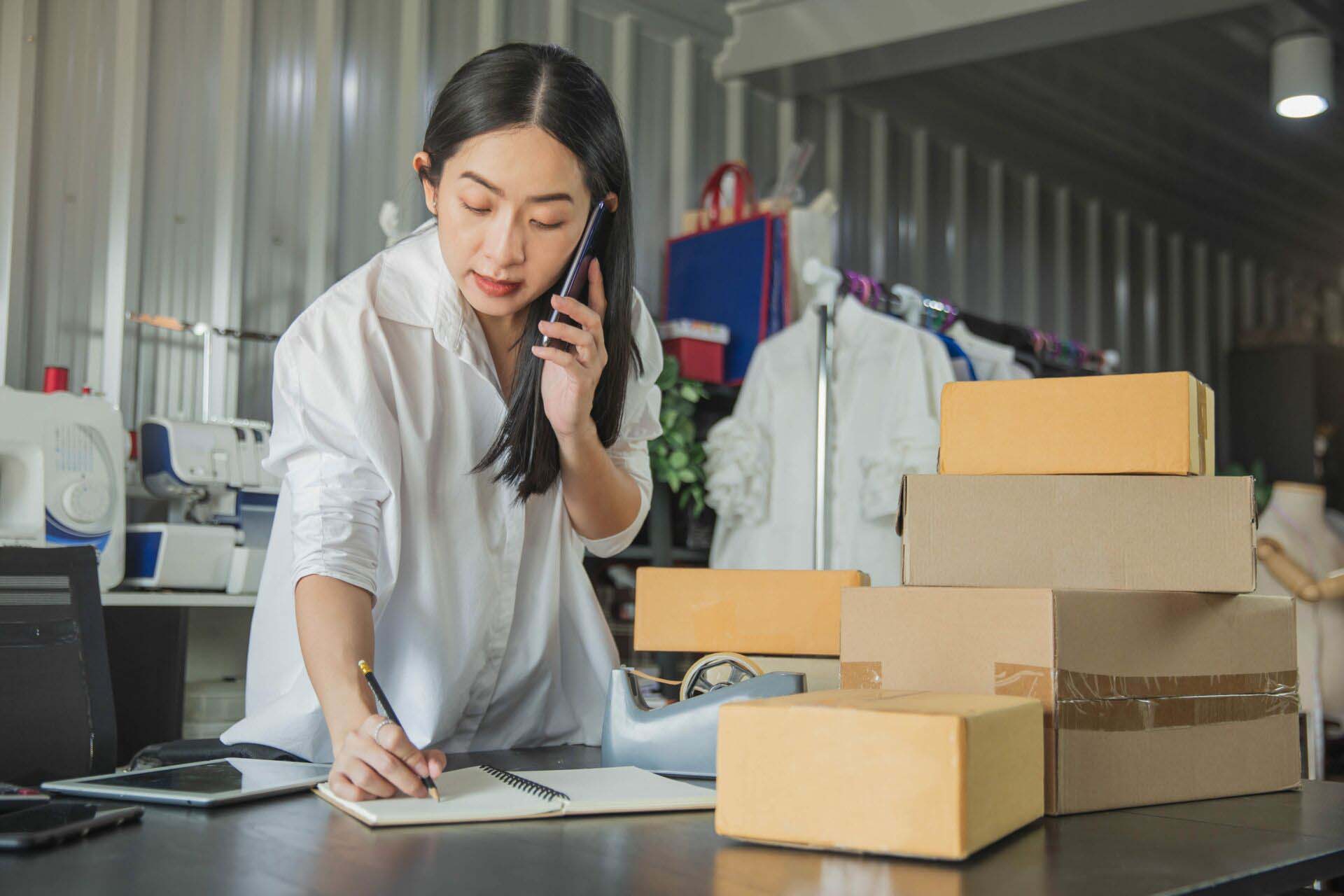 Young business woman working online e-commerce shopping at her shop. Young woman seller prepare parcel box of product for deliver to customer. Online selling, e-commerce. Insurance for E-commerce and Online Retailers