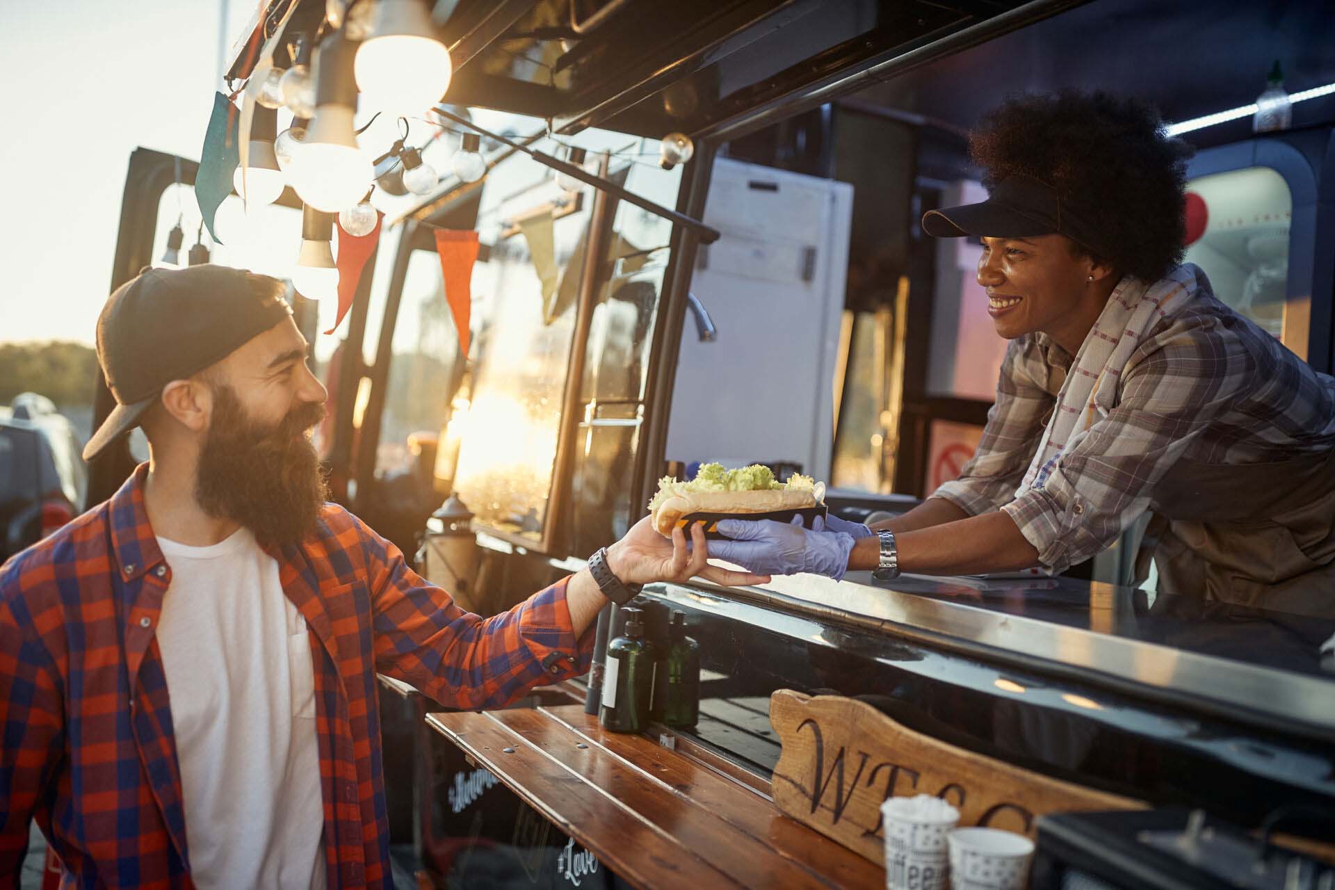 afro-american female employee gives with care sandwich to young Insurance for Food Trucks