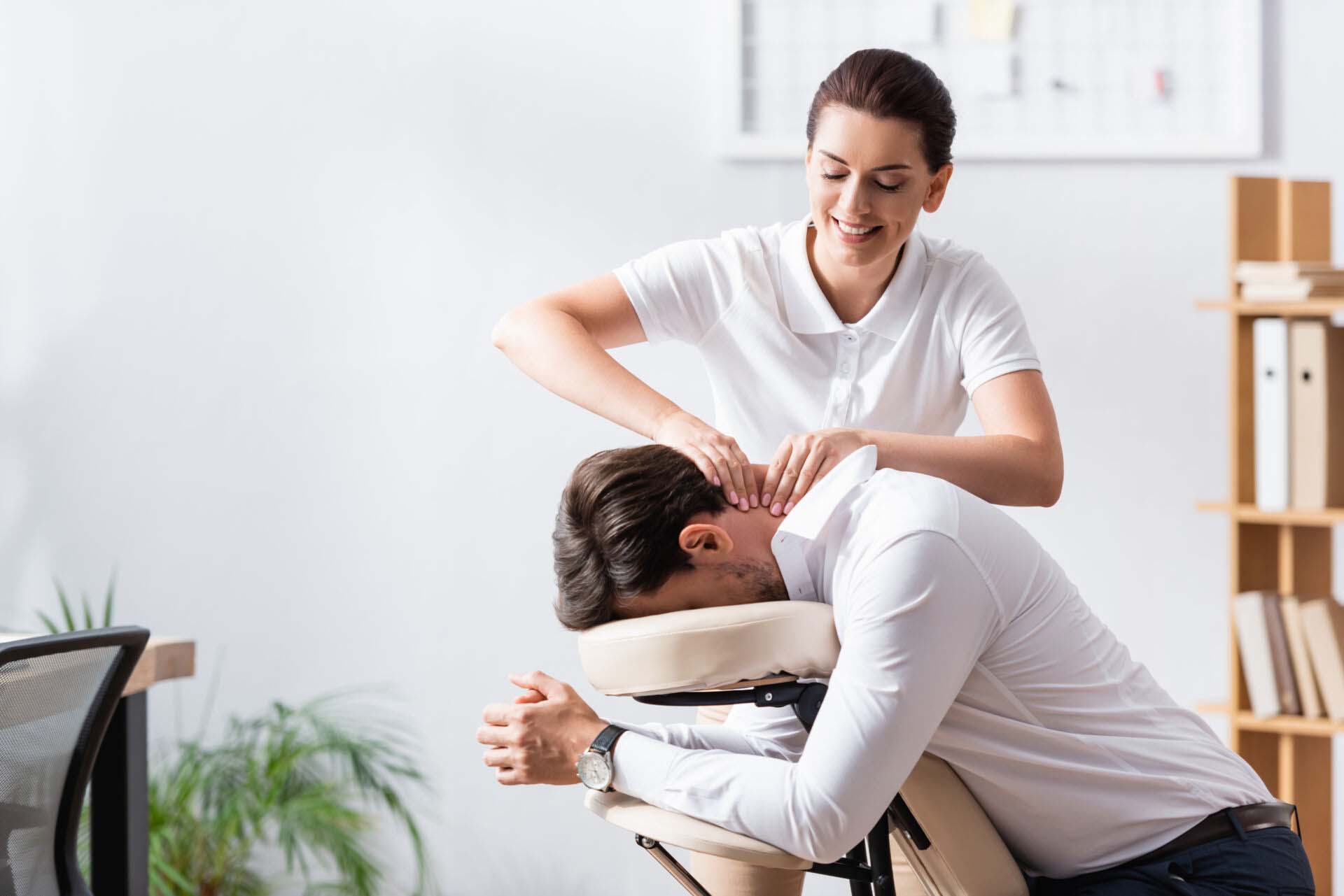 Happy masseuse doing neck massage for businessman in office on b Insurance for Massage Therapists