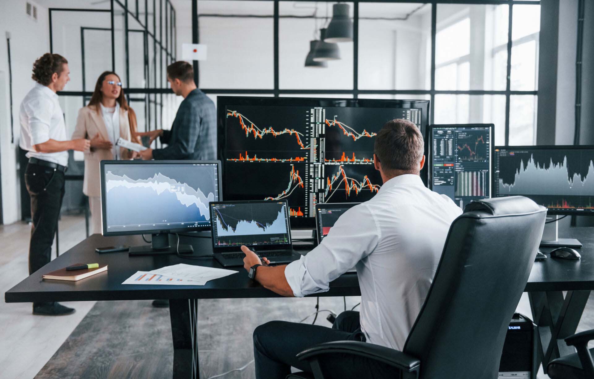 Ordinary office day. Team of stockbrokers works in indoors with many display screens Insurance for Stockbrokers