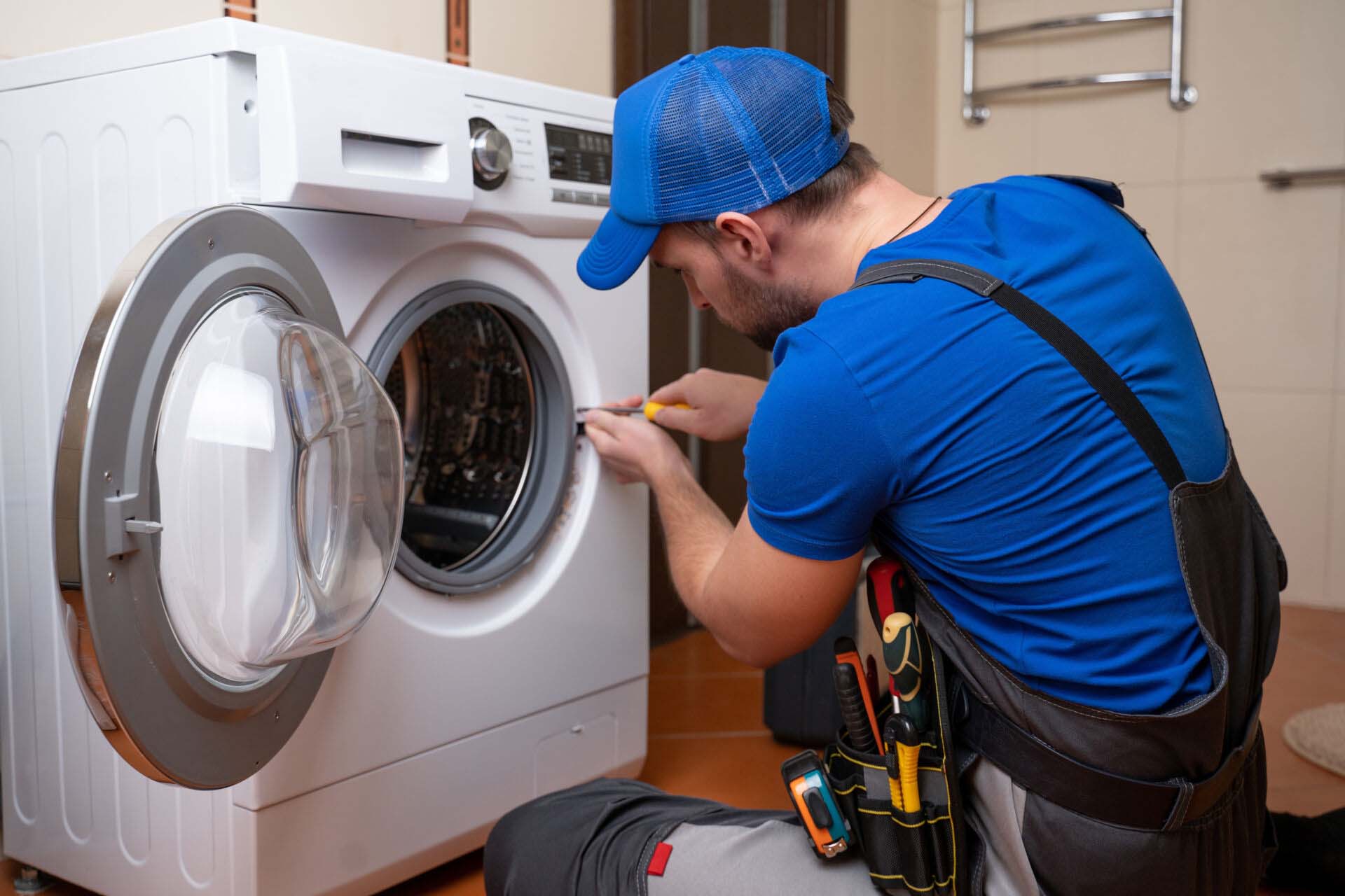 Working man plumber repairs a washing machine in home. Washing machine installation or repair. plumber connecting appliance Insurance for Appliance Repair Businesses