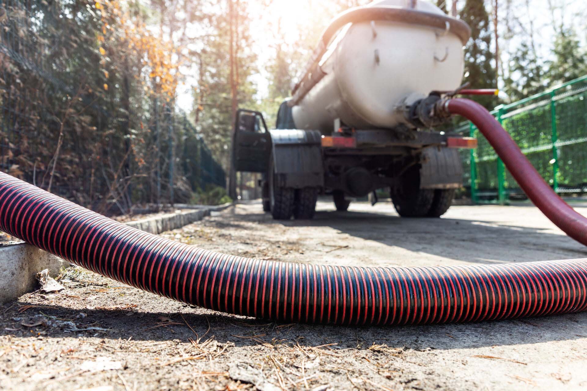 Close-up pipe hose of sewage truck car engine emptying home sewerage tank. Septic cleaning vacuum service and maintenance suburban countryside home. Suction vehicle cleaner machine pumping drainage Insurance for Septic Tank Cleaning Companies