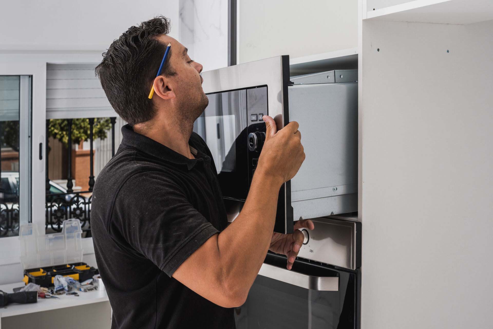 Man placing a microwave inside the hole of a new kitchen cabinet Installation