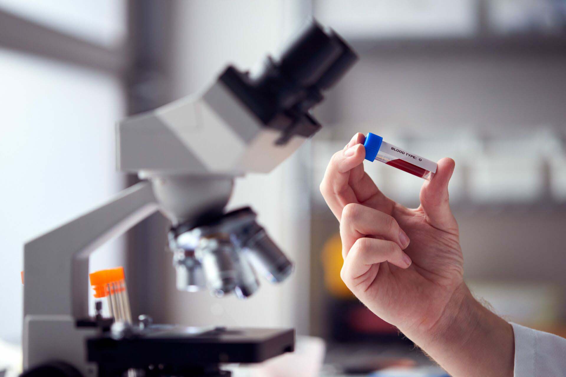 Close Up Of Male Lab Worker Or Phlebotomist Analysing Blood Samples In Laboratory With Microscope Insurance for Phlebotomists