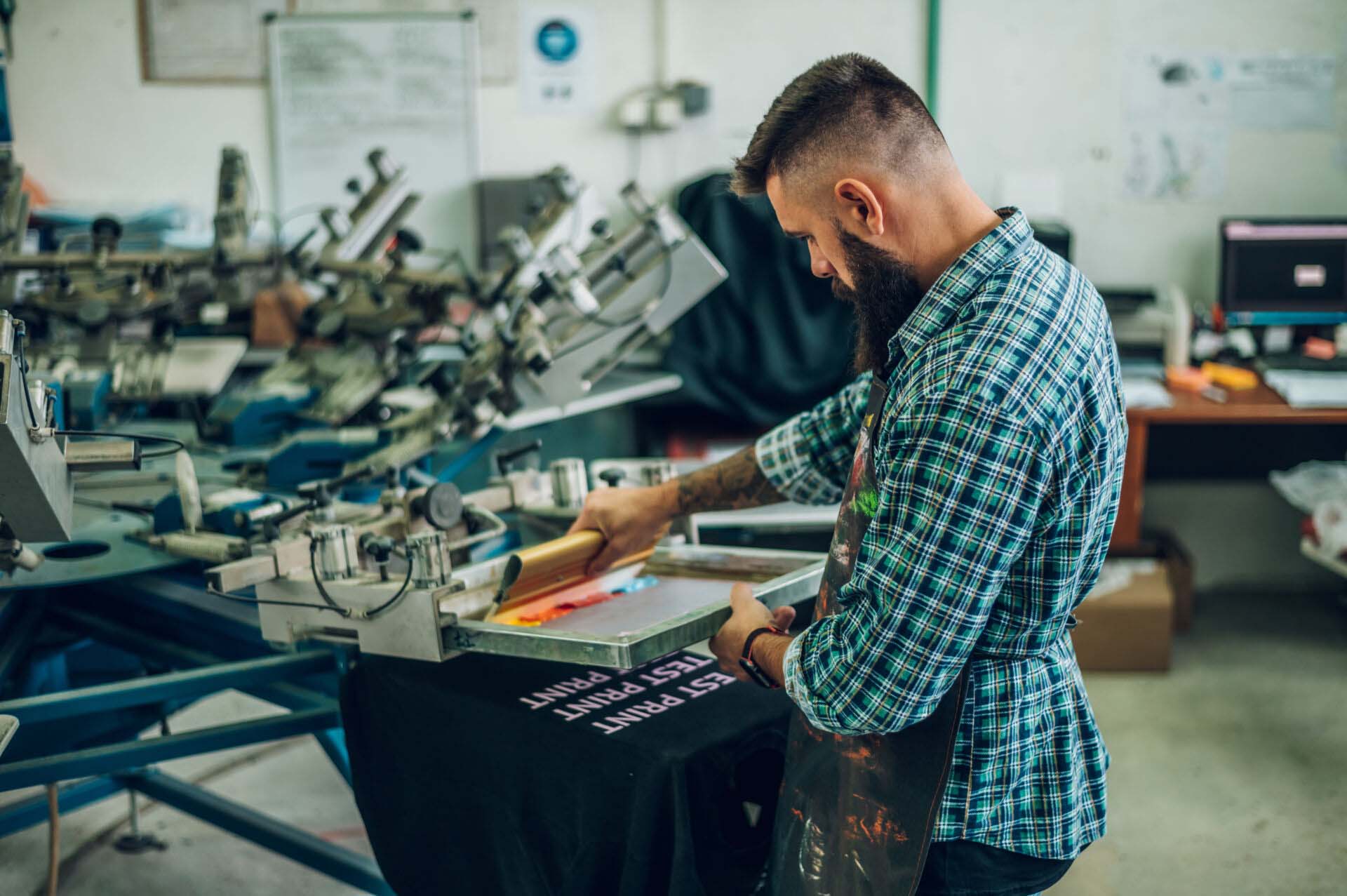 Male worker pressing ink on frame while using the printing machi Insurance for Screen Printing Businesses