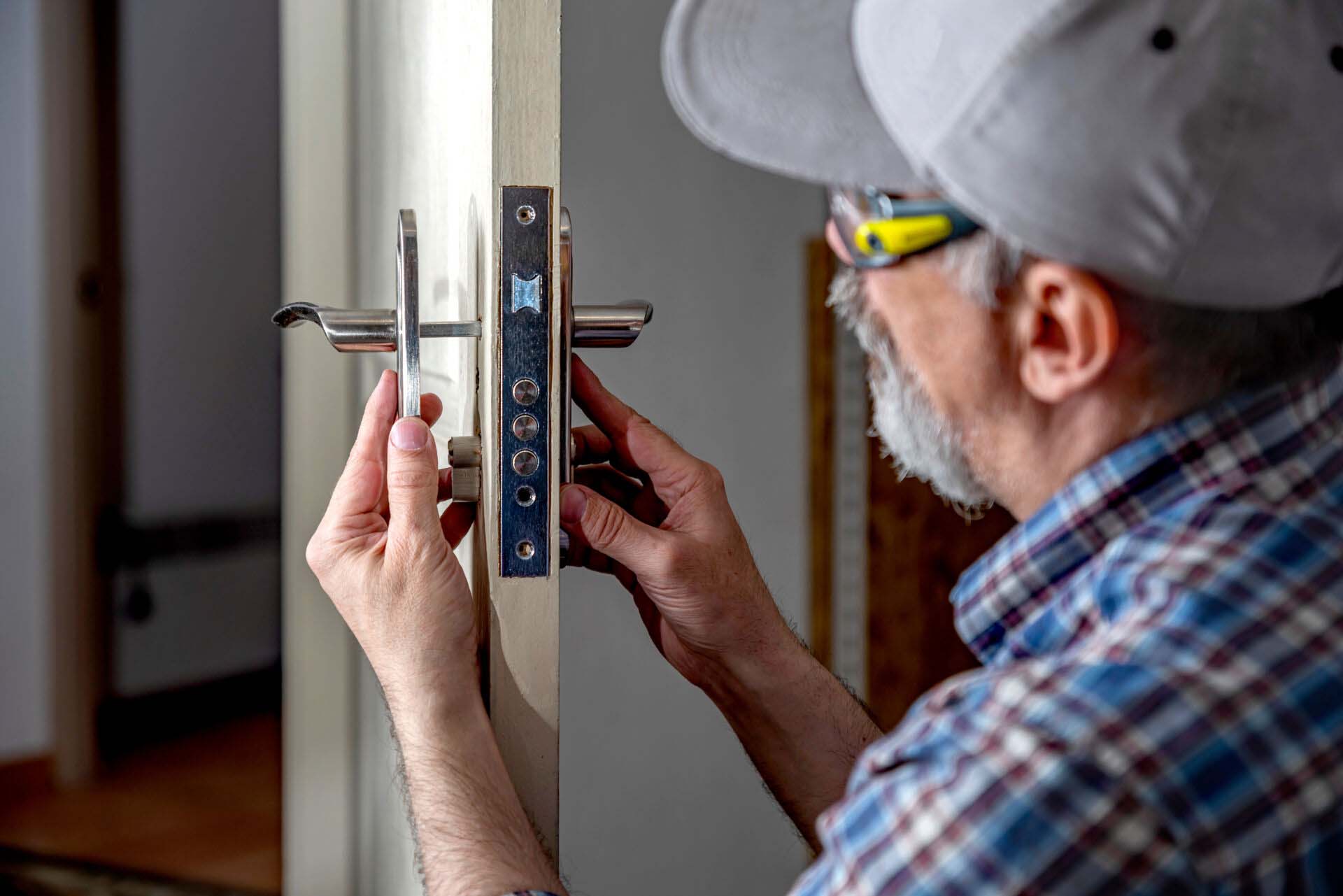 Door lock installation, repair, or replacement service. Door hardware installer locksmith working with open white door indoor Insurance for Locksmiths