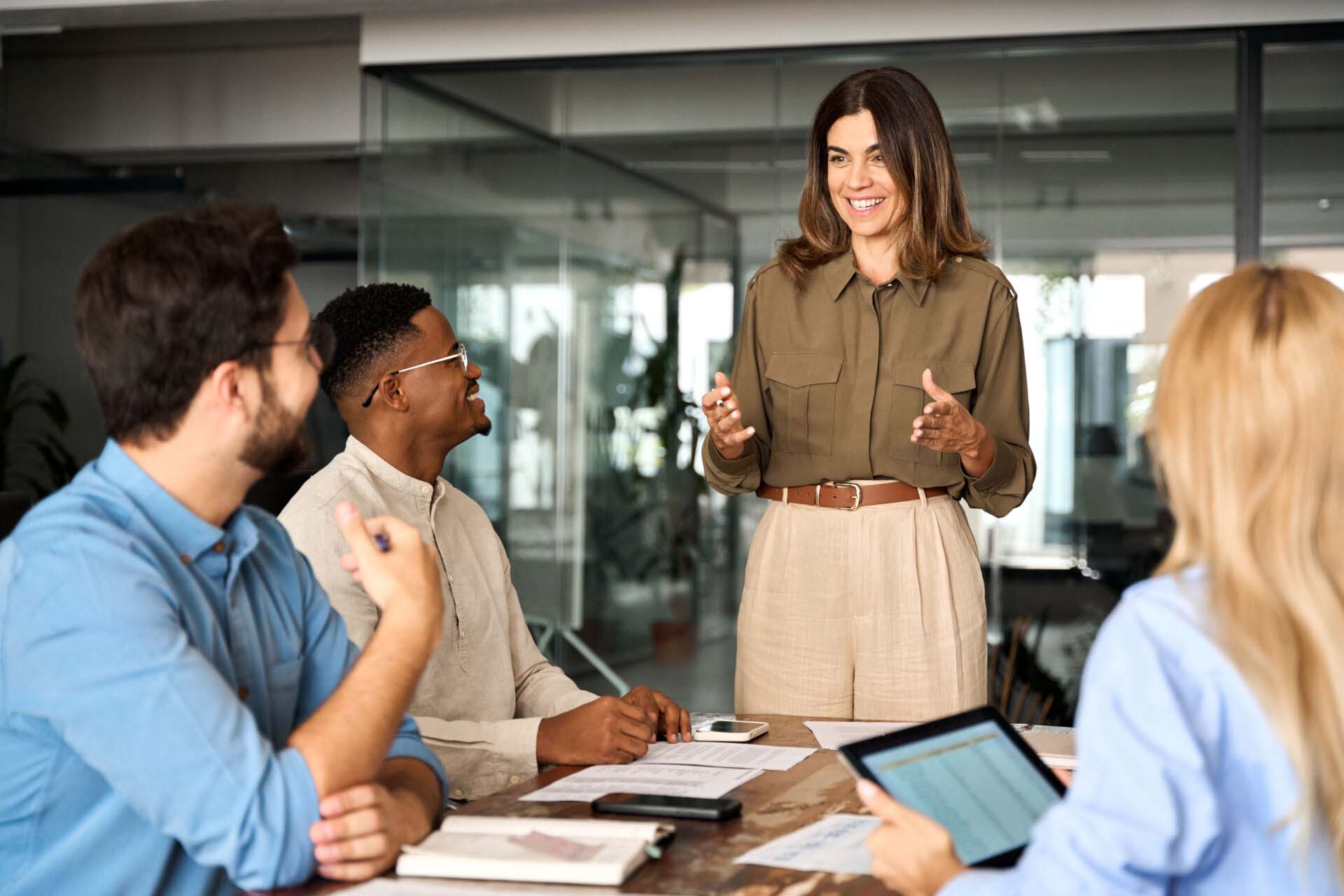 Happy middle aged business woman leader working with diverse team at meeting. Consulting