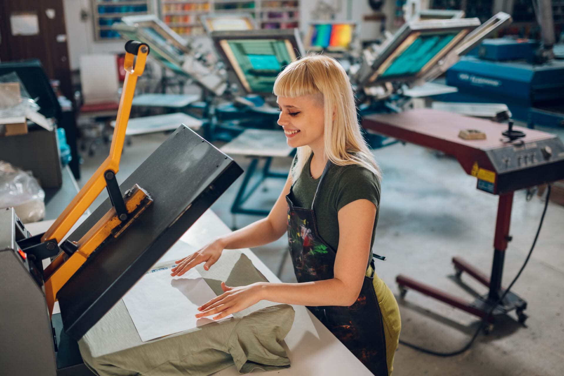 Smiling printing workshop worker using heating press and transfer on tee Printing and Copying