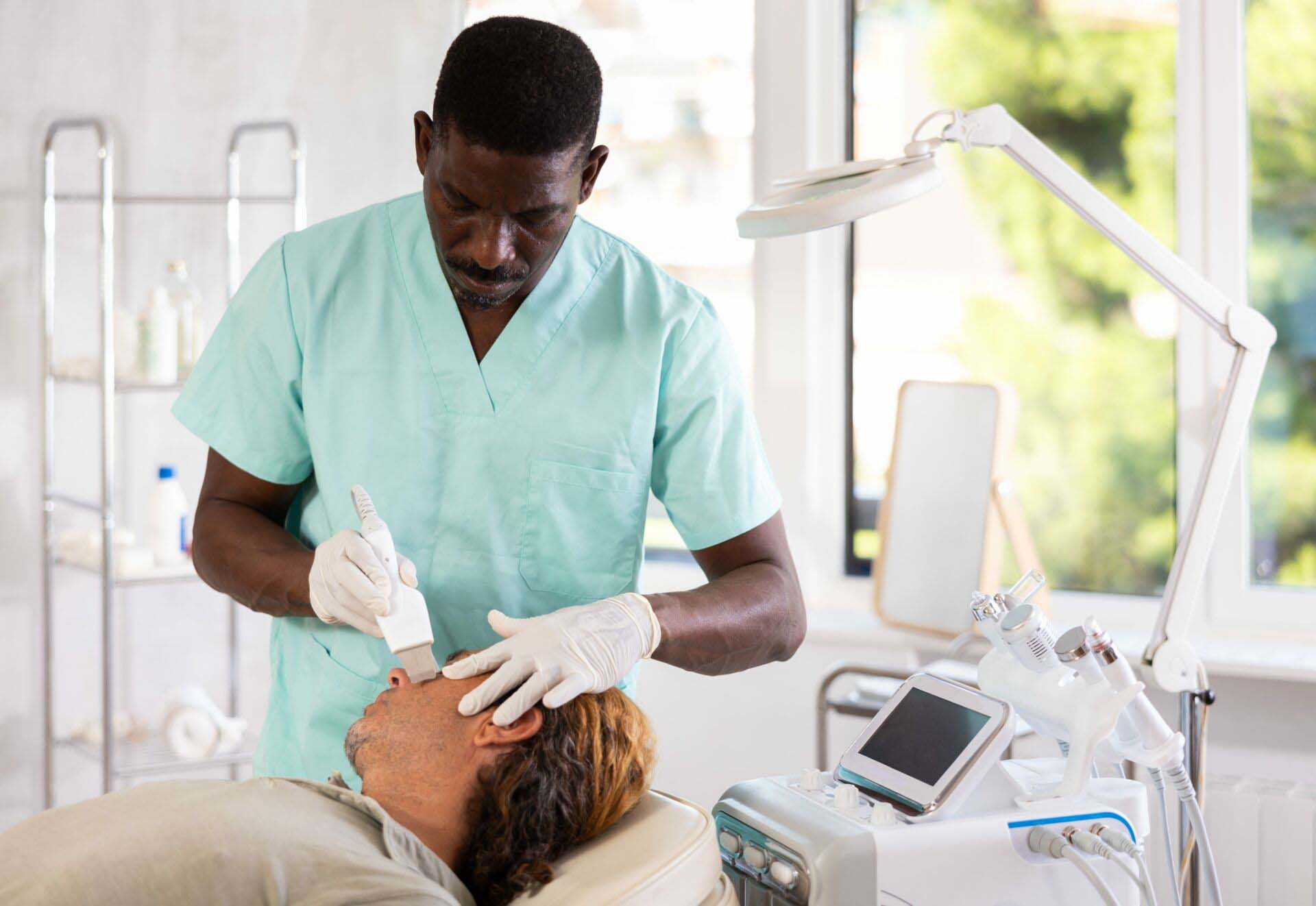 African American esthetician performing facial cosmetic treatment using ultrasonic shovel on man Insurance for Estheticians