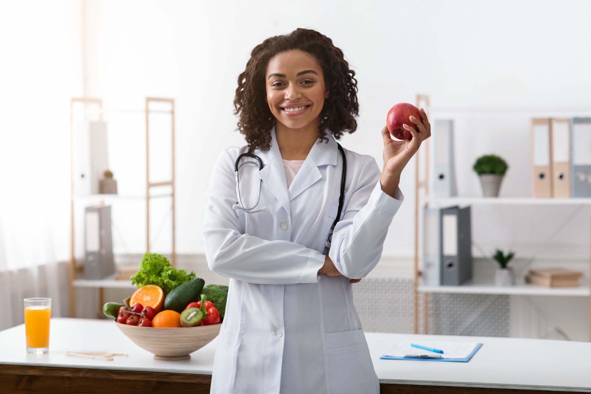 Pretty black lady dietologist holding apple in her hand Insurance for Dietitians