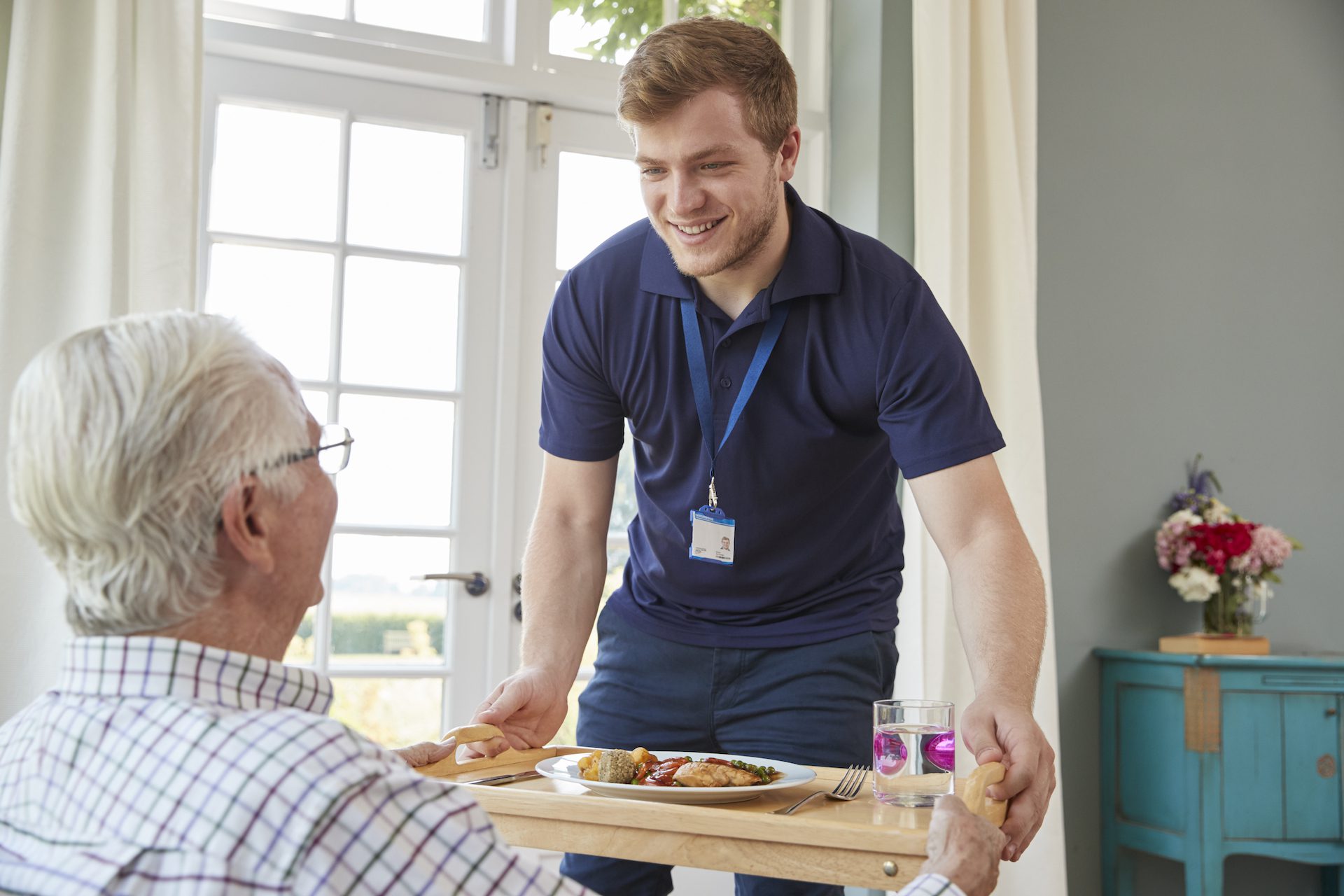 Male care worker serving dinner to a senior man at his home Assisted Living Facility
