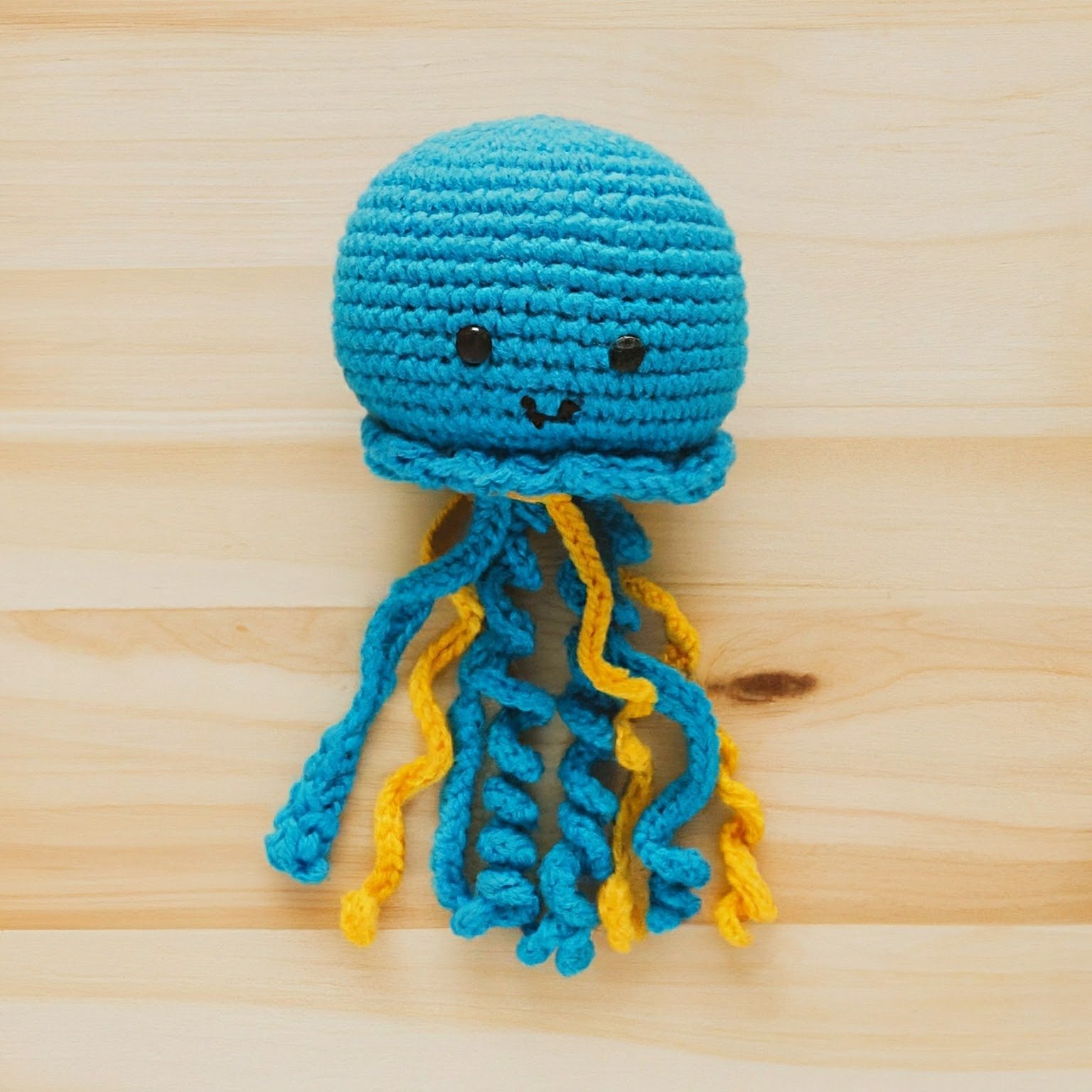 a cute jellyfish made with blue and yellow yarn, on light plywood table, overhead birds eye view
