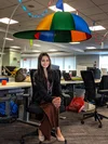 Snehal sitting at a desk with a large structure above her shaped like a colorful hat with a propeller.