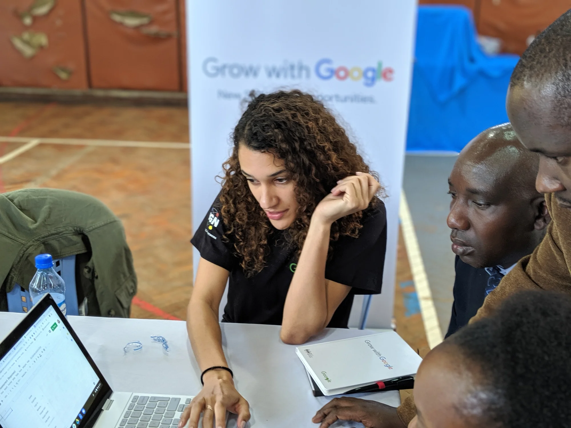 A Googler sits with a group of small business owners attending the training. The Googler is showing how to use Google Sheets on a laptop for the group as they watch the screen.