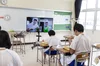 A group of students sitting at their desks in a classroom having a meal, while watching a video on a screen at the front of the room