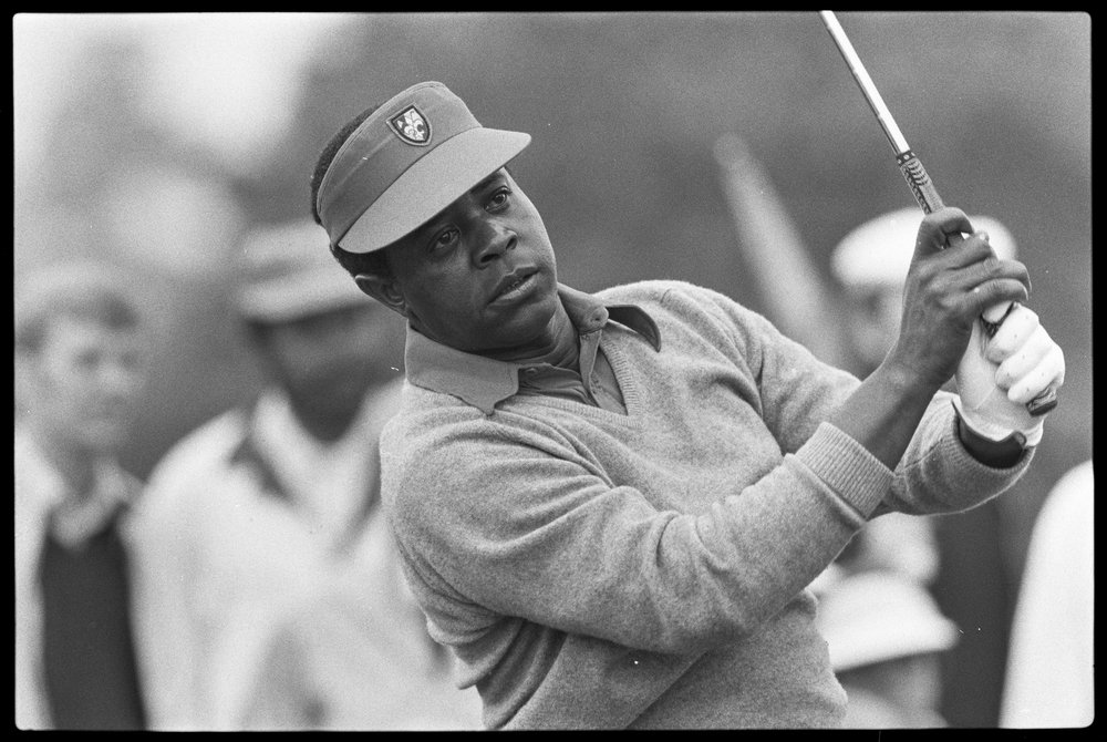 This is a black and white photo from 1975 of Lee Elder swinging a golf club at a major competition.