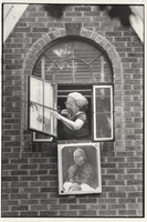 A woman closing her window with a picture of the Pope hanging off of the window pane.