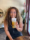 A woman sits in a cafe sipping bubble tea and smiling.