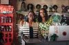 Two women look straight at the camera behind a counter. The words "Beauty Salon" are in neon behind them. Along the back wall are a variety of wigs on mannequin heads.