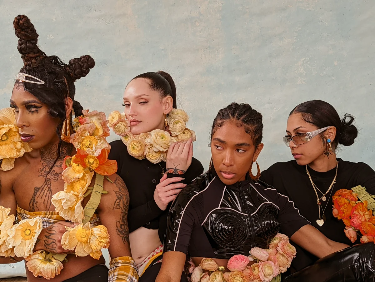 Photograph of four people with flowers draped around them. They're all looking to the right of the camera lens.