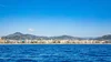 Zdjęcie Morza Śródziemnego. W tle linia brzegowa miasta Nicea, szczyty wzgórz i słoneczne niebo.