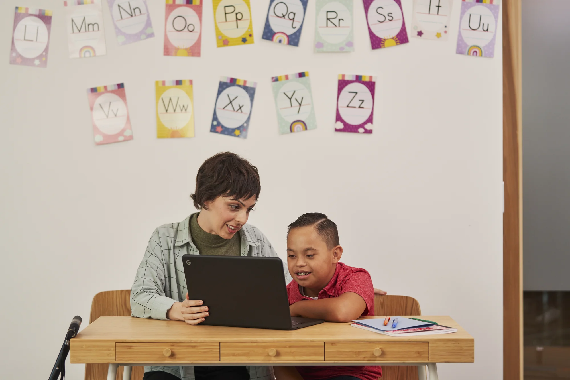 A teacher sitting with a student with intellectual disabilities. The teacher's cane is leaning on the table nearby.