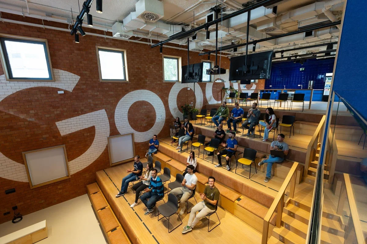 Fotografía de 17 personas sentadas en un aula cuya pared dice Google.