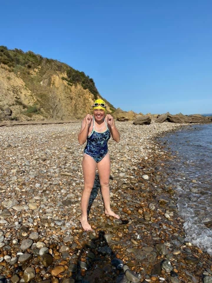 A woman in a bathing suit and swim cap celebrating on a rocky beach.