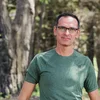Zdjęcie Alexa Frenkla, dyrektora generalnego i współzałożyciela Kai.ai, na zdjęciu od pasa w górę w plenerze. Ma na sobie okulary i zieloną koszulkę.