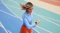 Image of a woman runs on a track. On the right, an up-close view of Pace Training on Pixel Watch 2 with the Coral Active Sport Band.