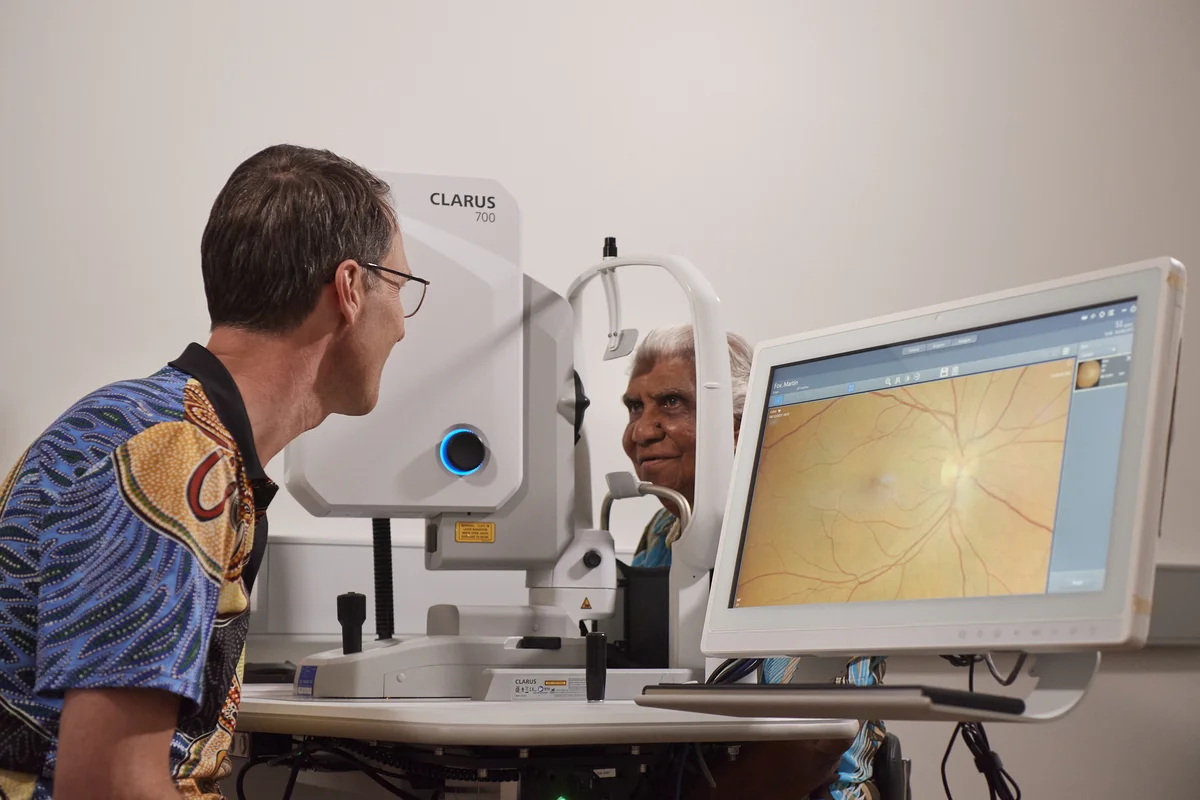 A photo of Dr Angus Turner examining retinal images of a patient sitting opposite him, via a computer screen