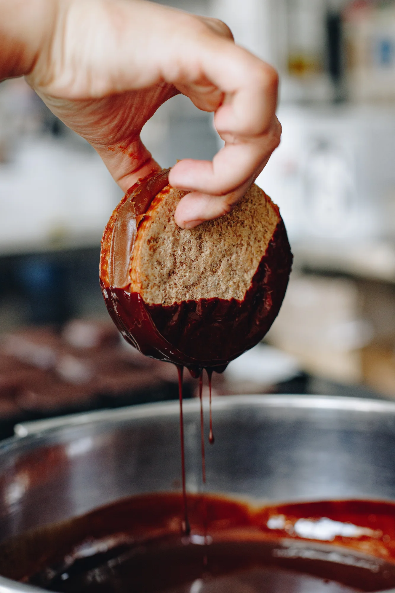 A hand dips a dulce de leche filled  alfajor cookie sandwich into chocolate.