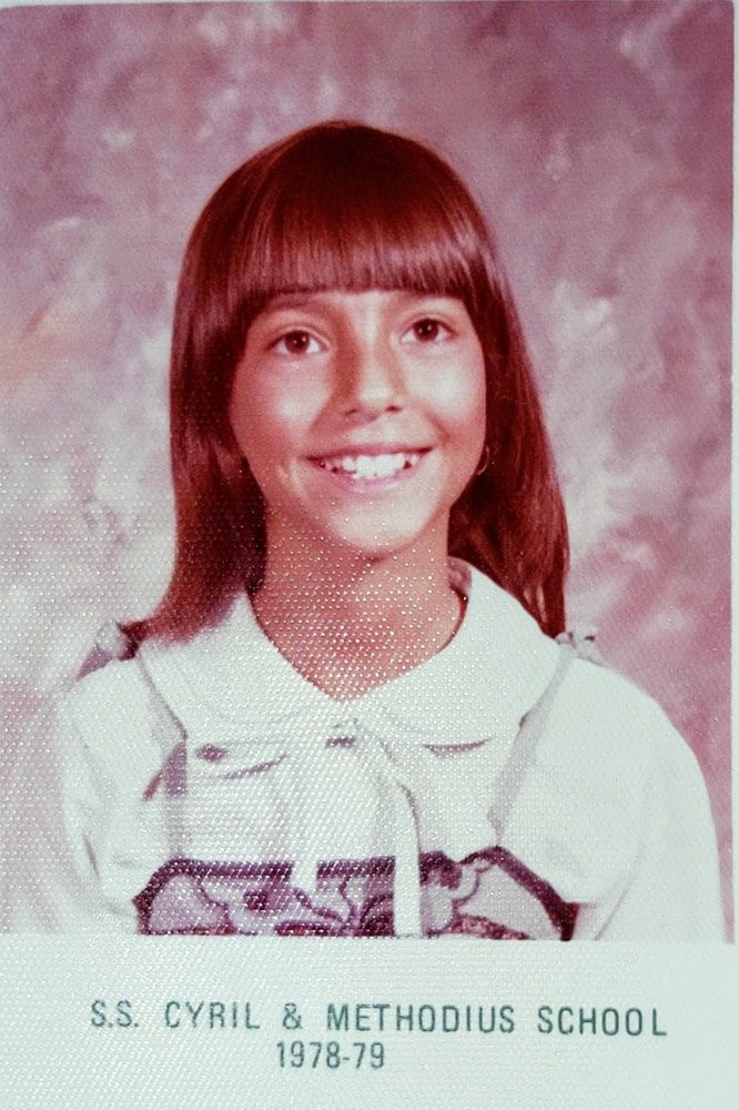 A young Monica smiling at the camera. She is wearing a white collared shirt and posing for her 3rd grade photo.