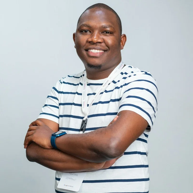 A man wearing a white and black striped shirt smiles at the camera, with his arms crossed across his chest.