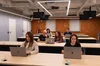 Fotografía de 6 personas sentadas en escritorios de universidad con ordenadores portátiles.