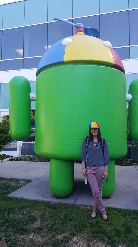 Emily standing next to a large Android statue with a Noogler hat.