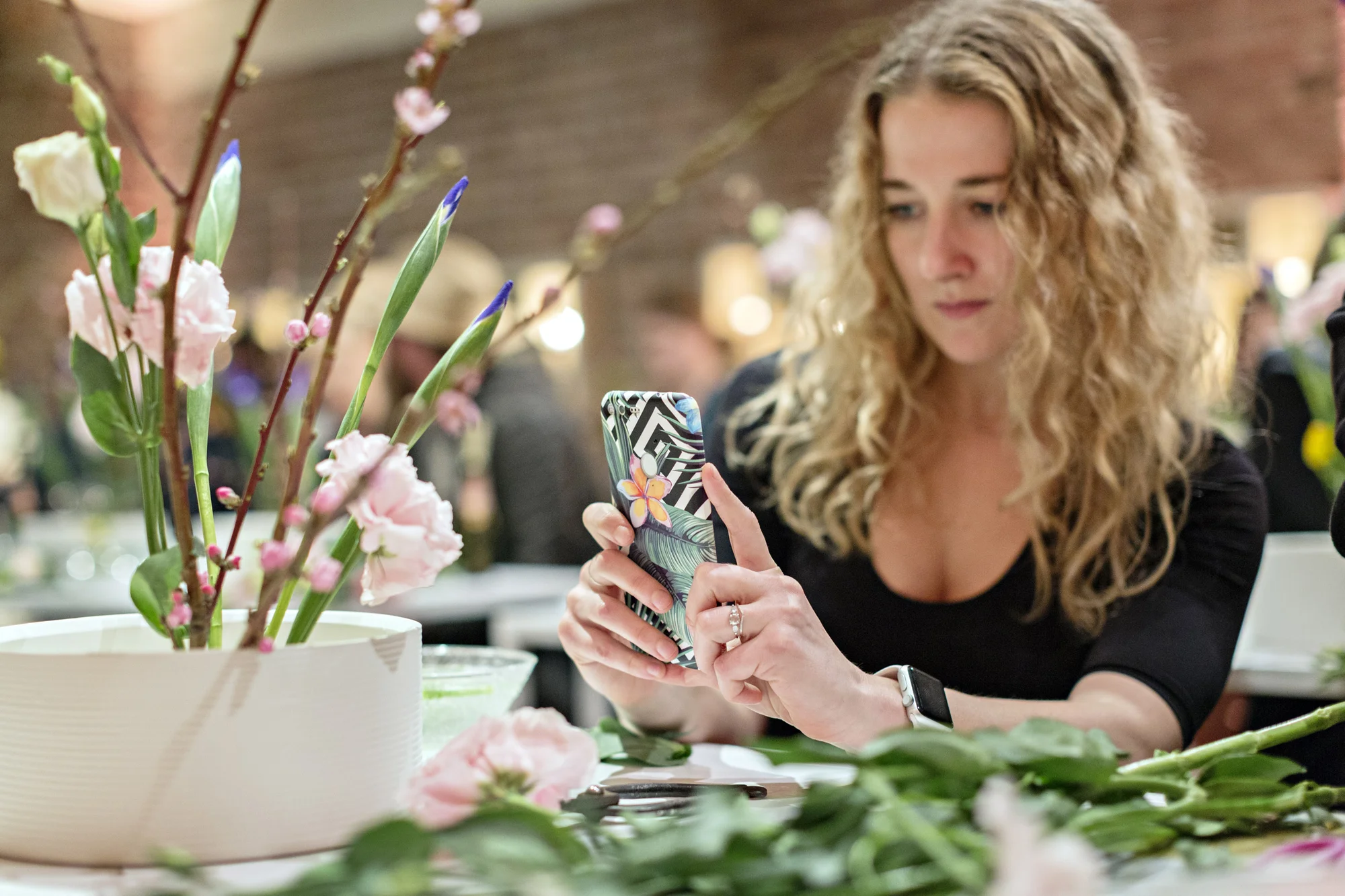 A person with blond hair taking a photo of a flower arrangement