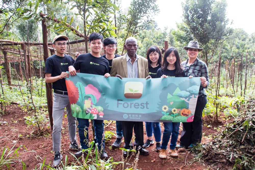A group of seven people standing outside and holding a banner that says “Forest.”