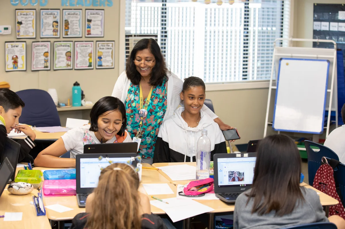 An educator works with her two middle school students on computer science lessons in the classroom.