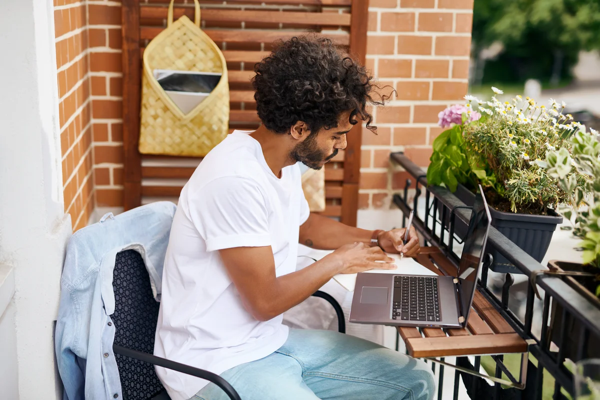 Auf dem Foto sieht man einen jungen Mann an einem Tisch vor einem aufgeklappten Laptop sitzend.