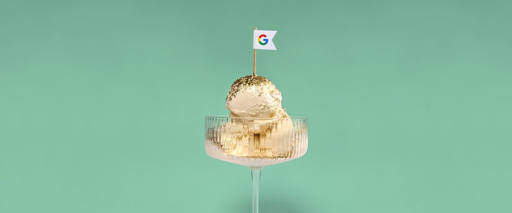 A dish of vanilla ice cream with golden glitter sprinkles and a toothpick flag with a Google logo on it