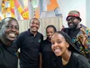 A group of five Googlers, all in black t-shirts with a multi-colored logo, pose together and smile at the camera.