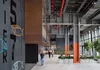 A double height interior space is shown with steel beams and concrete floors with a Pier 57 logo painted on the wall and people walking down the hallway.