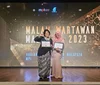 Two people standing on a stage, holding awards and smiling.