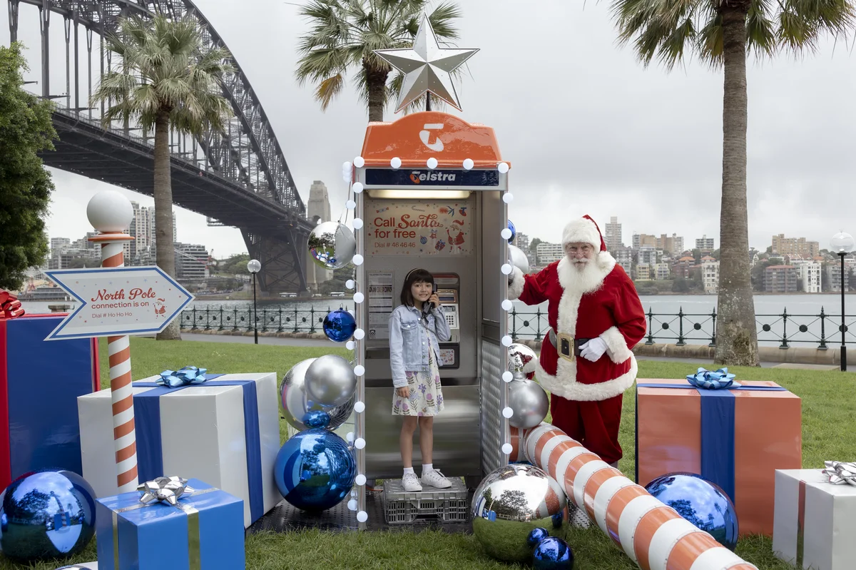 Santa and a young girl standing next to a phone booth
